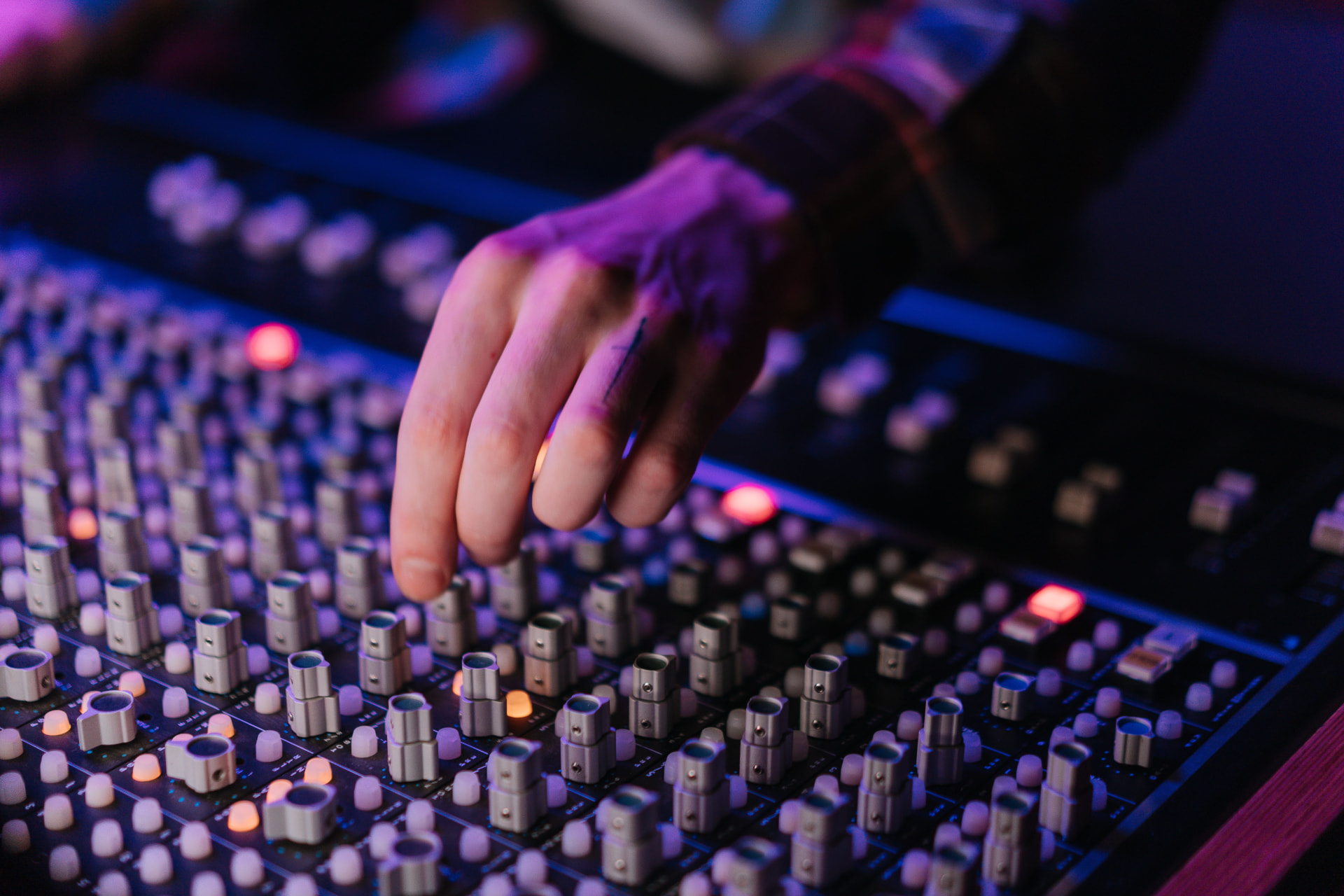 Hand adjusting faders on a lit audio mixing console in a live venue